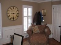 Cozy living room corner with armchair, wall clock, window shutters, and white door