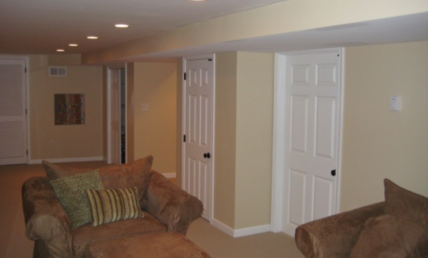 Living room with tan sofas, beige walls, white doors, and recessed ceiling lights.