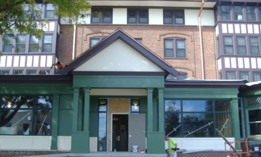Front entrance of a green-trimmed brick building with large windows and a covered porch