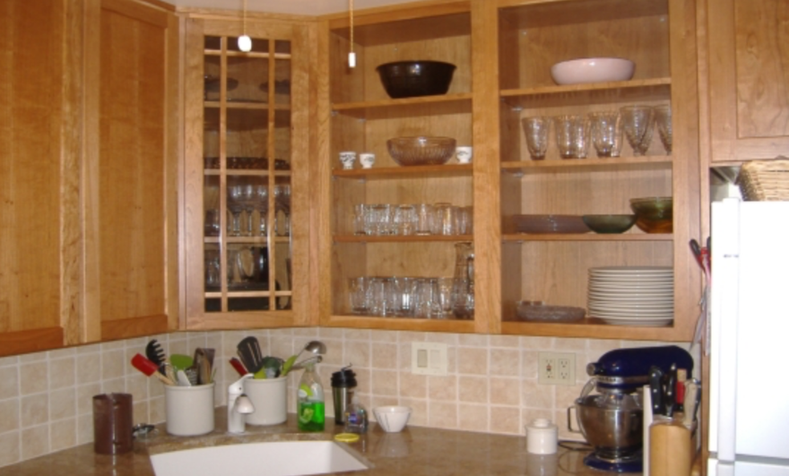 Wooden kitchen cabinets with glassware, bowls, and dishes above a tiled countertop