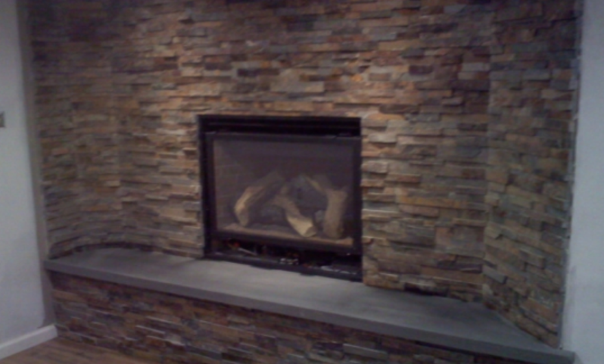 Stone fireplace with a dark firebox set into a stacked-stone wall and a curved hearth bench