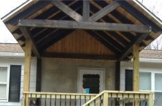 Front porch with wooden gabled roof, white siding, and a black railing on a house.