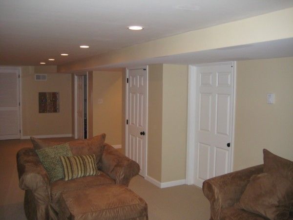 Cozy basement living room with beige walls, recessed lights, and brown armchairs near white doors