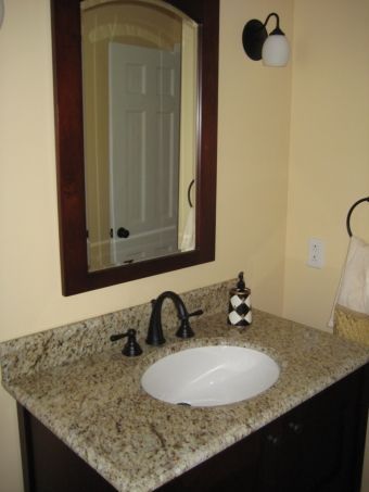 Bathroom vanity with granite countertop, oval sink, mirror, and wall light next to a beige wall.