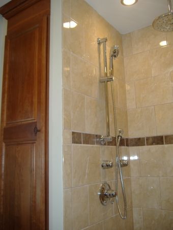 Shower stall with beige tile, chrome showerhead, and a wooden bathroom door beside it