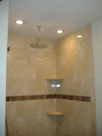 Tiled walk-in shower with ceiling lights, showerhead, corner shelf, and brown accent tile strip