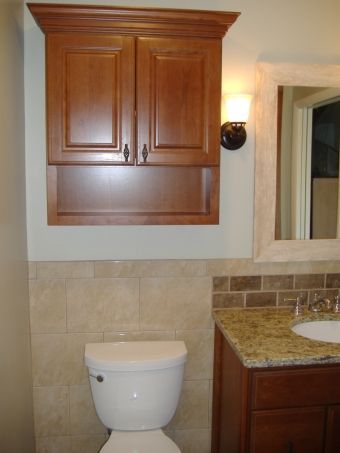 Bathroom with wall-mounted wood cabinet above a toilet and a granite vanity with sink on the right.