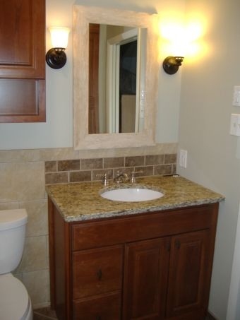 Small bathroom vanity with granite countertop, round sink, mirror, wall sconces, and a toilet edge visible.