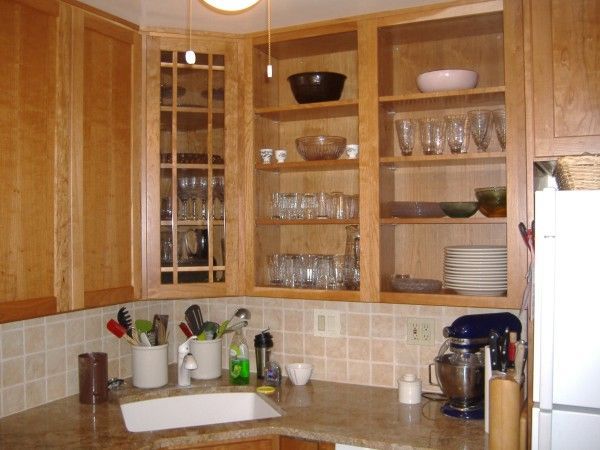 Wooden kitchen cabinets with glass doors, dishes, and countertop appliances on a beige counter