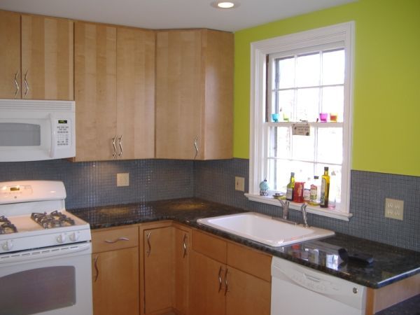 Modern kitchen with light wood cabinets, white appliances, dark countertop, and a window over the sink.