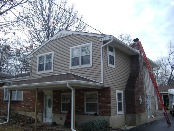 Two-story beige house with white trim and a red ladder leaning against the roof on a cloudy day