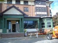 Green-trimmed building entrance with a white van, construction equipment, and a worker in front