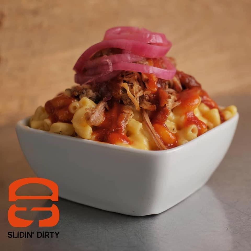 Mac and cheese bowl with pulled pork, sauce, and pickled onions; logo in corner.