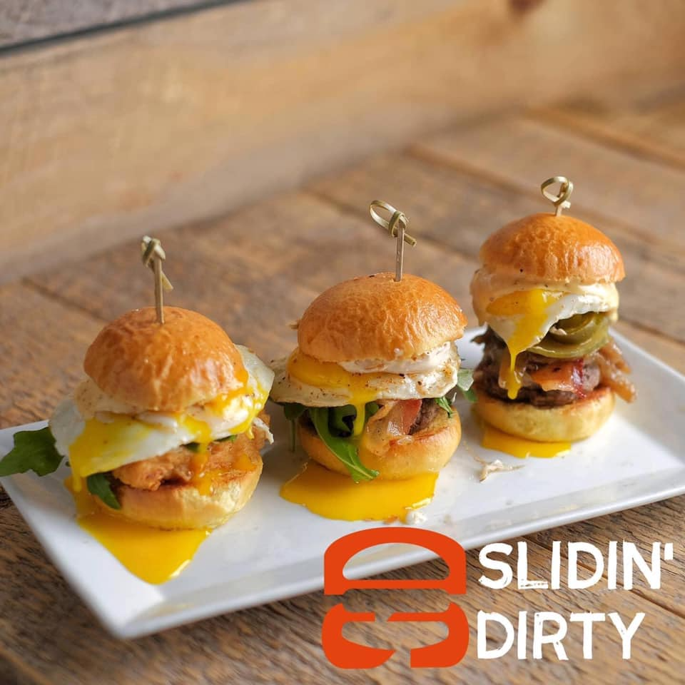 Three sliders on a white plate, each with a fried egg and toppings. A