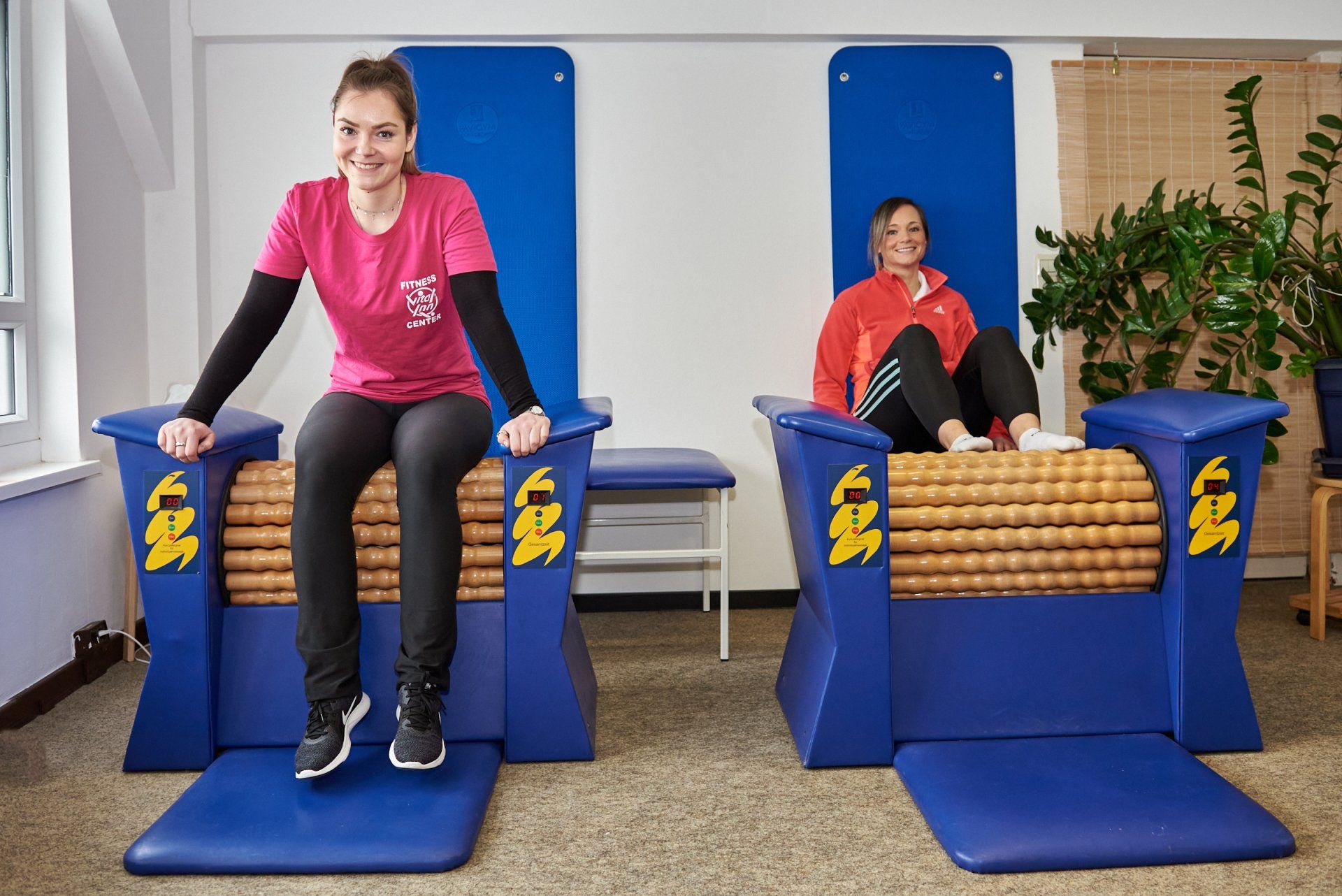 Zwei Frauen sitzen in einem Fitnessstudio auf Massagestühlen.