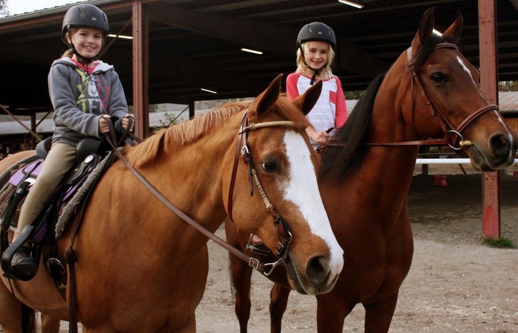 Two young girls are riding horses in a stable