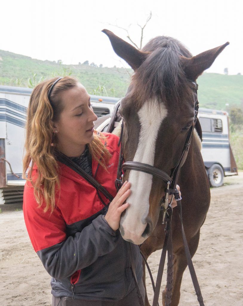 A woman in a red jacket is petting a brown horse