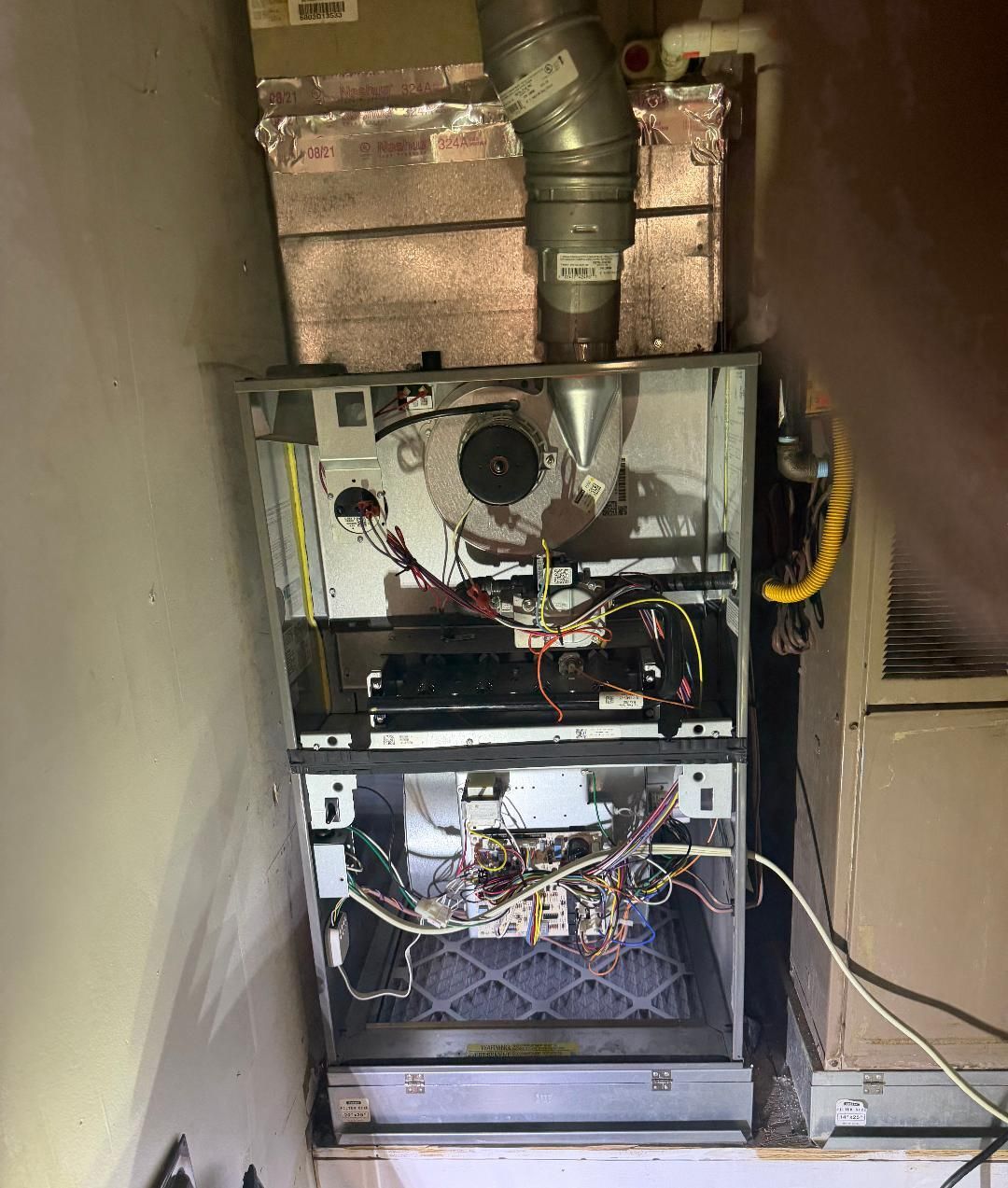 Open furnace and wiring in a utility closet with exposed ducts and cables