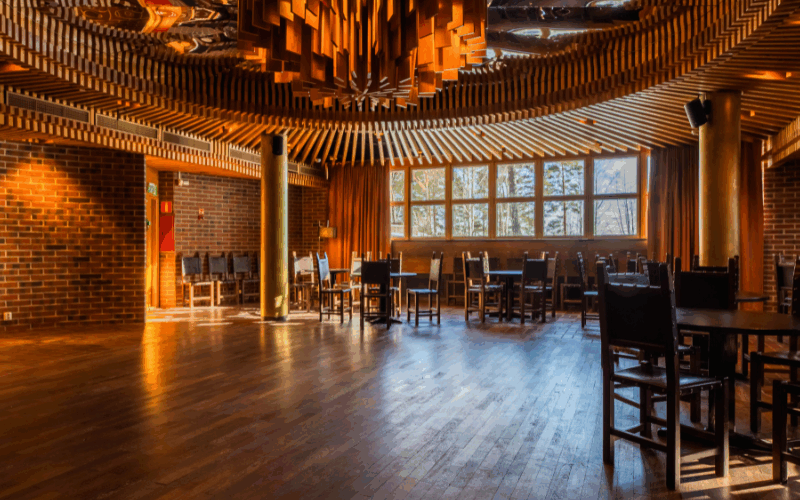 An elegant restaurant interior with dark wooden floors, brick walls, gold pillars, and a unique radial wood-slat ceiling.
