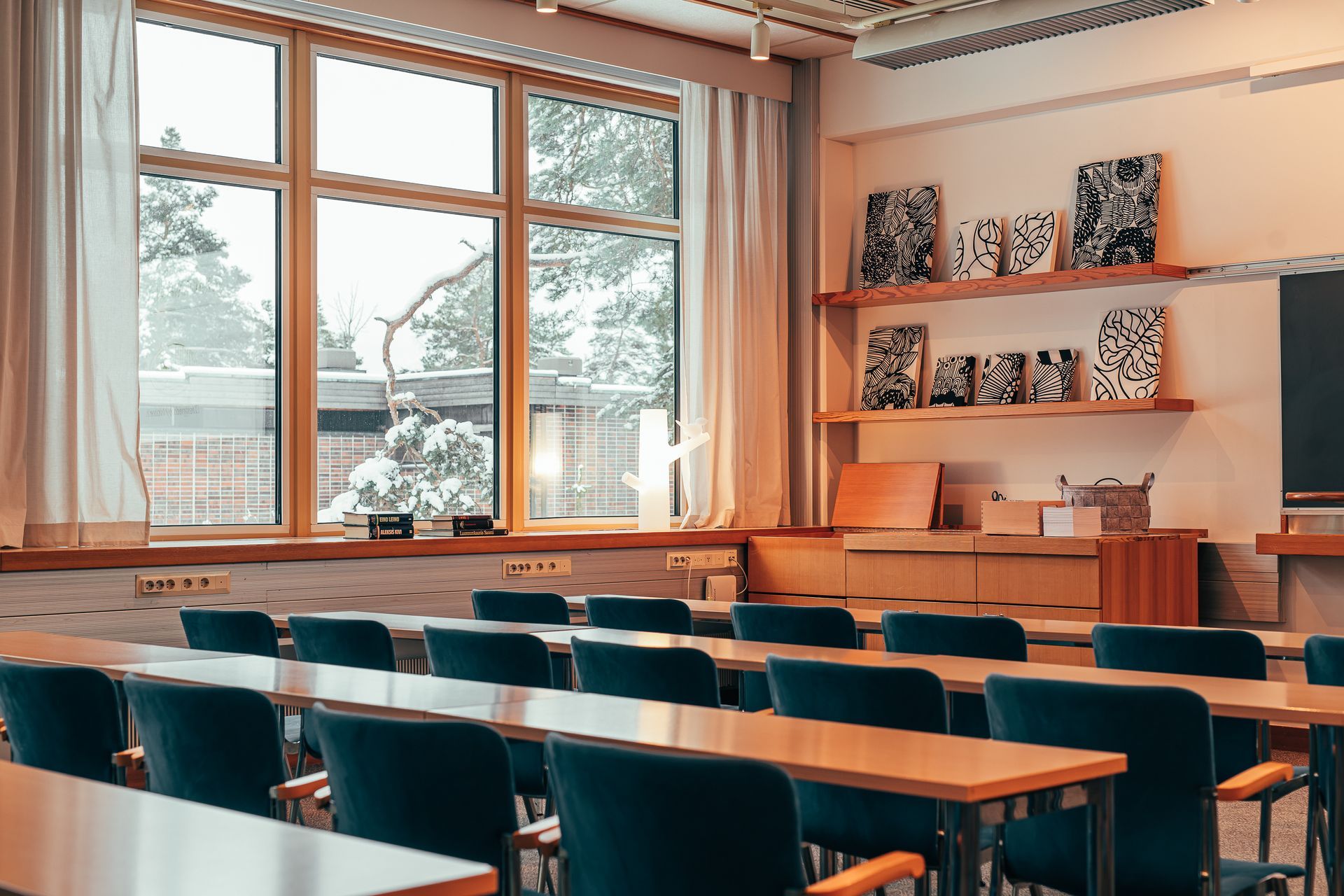 A classroom with rows of dark chairs facing front, wooden tables, and shelves decorated with patterned tiles.