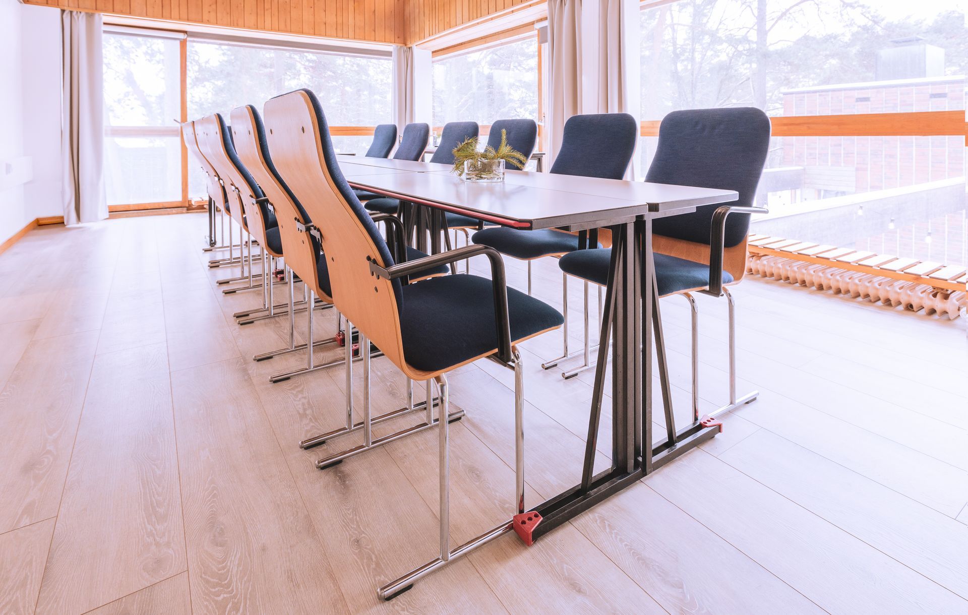 A row of dark office chairs and a long conference table in a bright room with light wood floors and large windows.