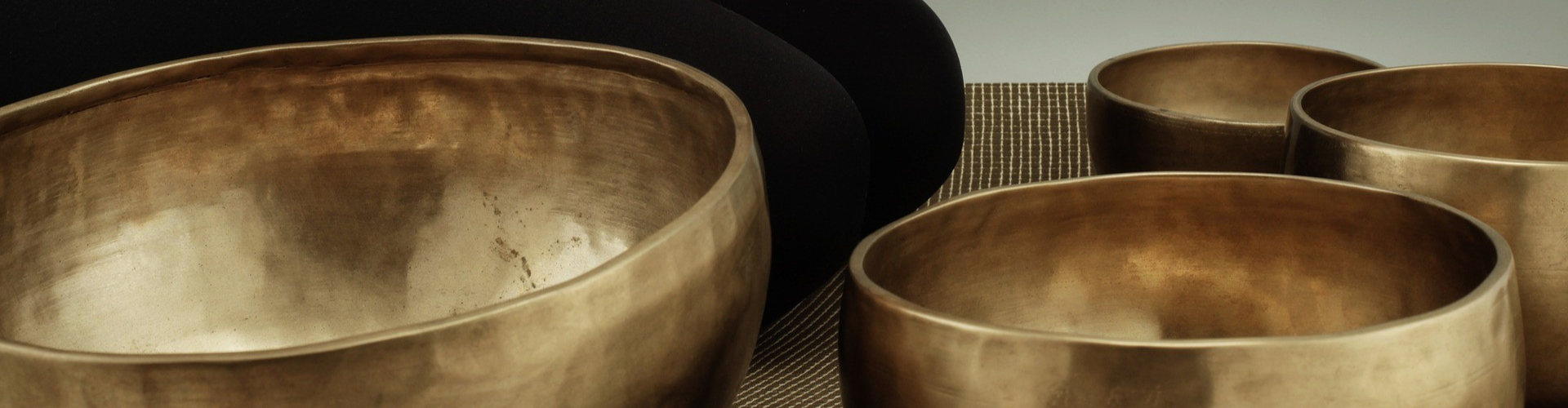 Several metallic singing bowls arranged on a textured surface.