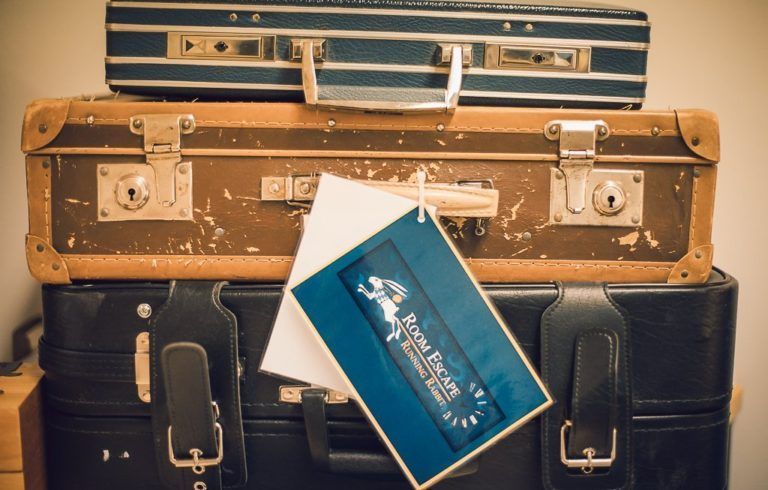 A stack of three vintage suitcases with a Room Escape branding tag hanging from the middle case.