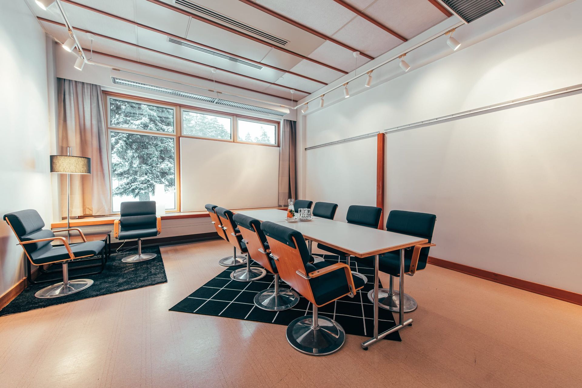 A bright, modern meeting room with a long table, eight black ergonomic chairs, large windows, and a white presentation board.