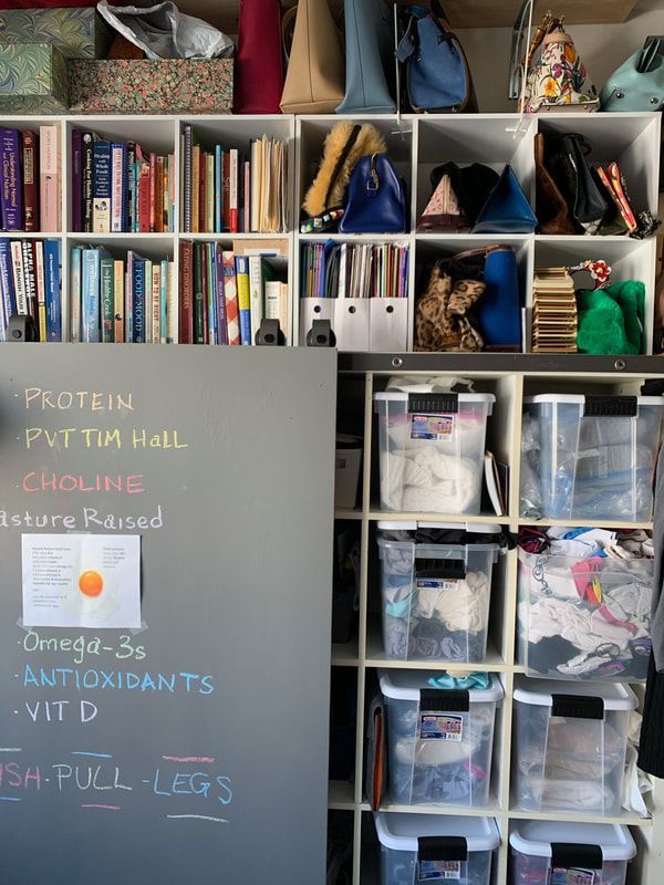 A chalkboard with colorful notes is next to a built-in shelving unit filled with books, bins, and bags.