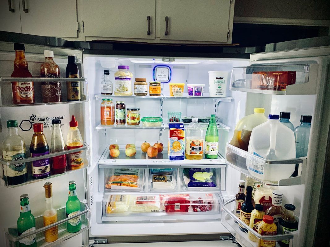Open refrigerator filled with condiments, fruits, and beverages. Bright lighting against white interior.
