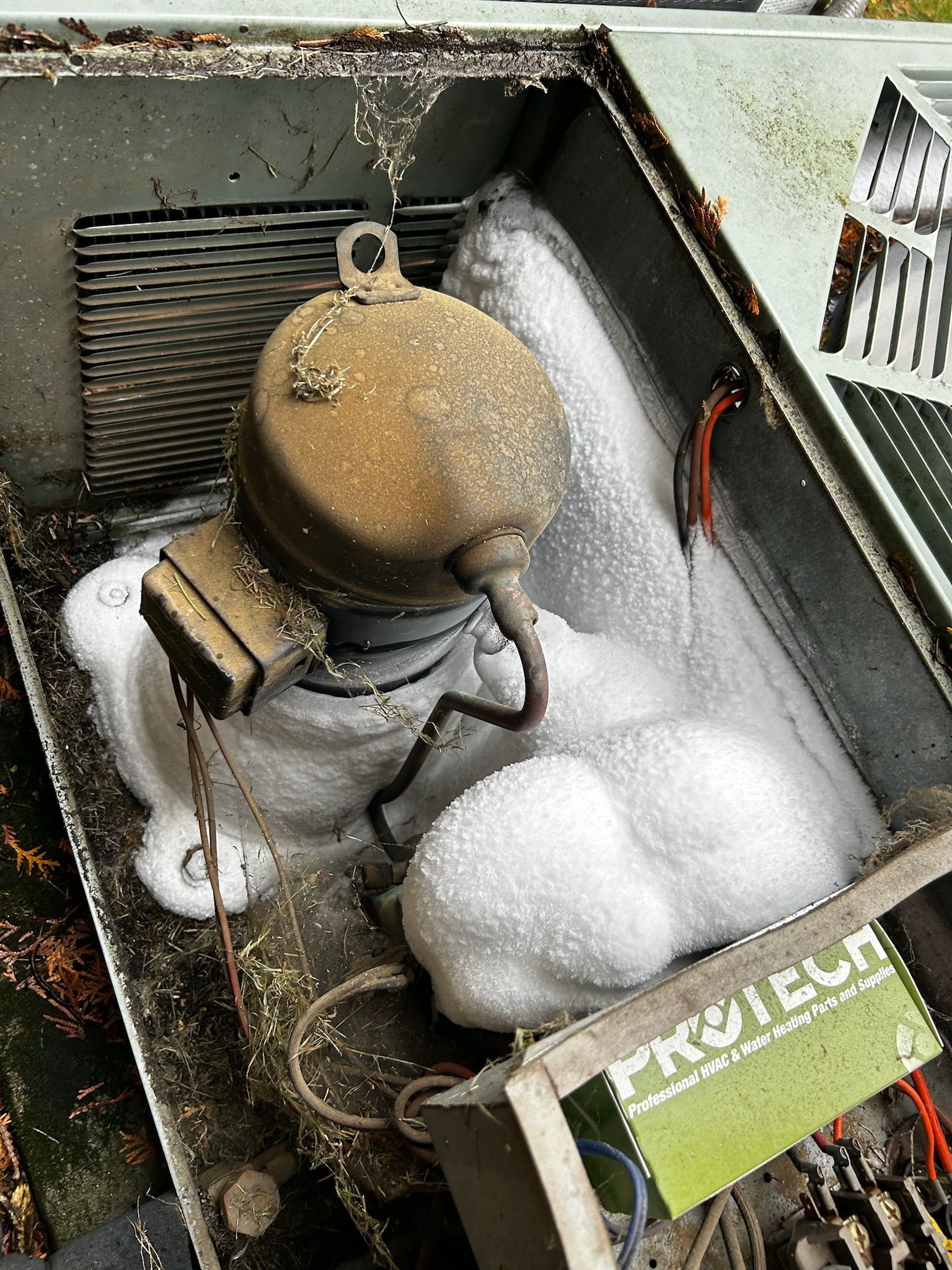 Air conditioner unit covered in ice and frost, components visible.