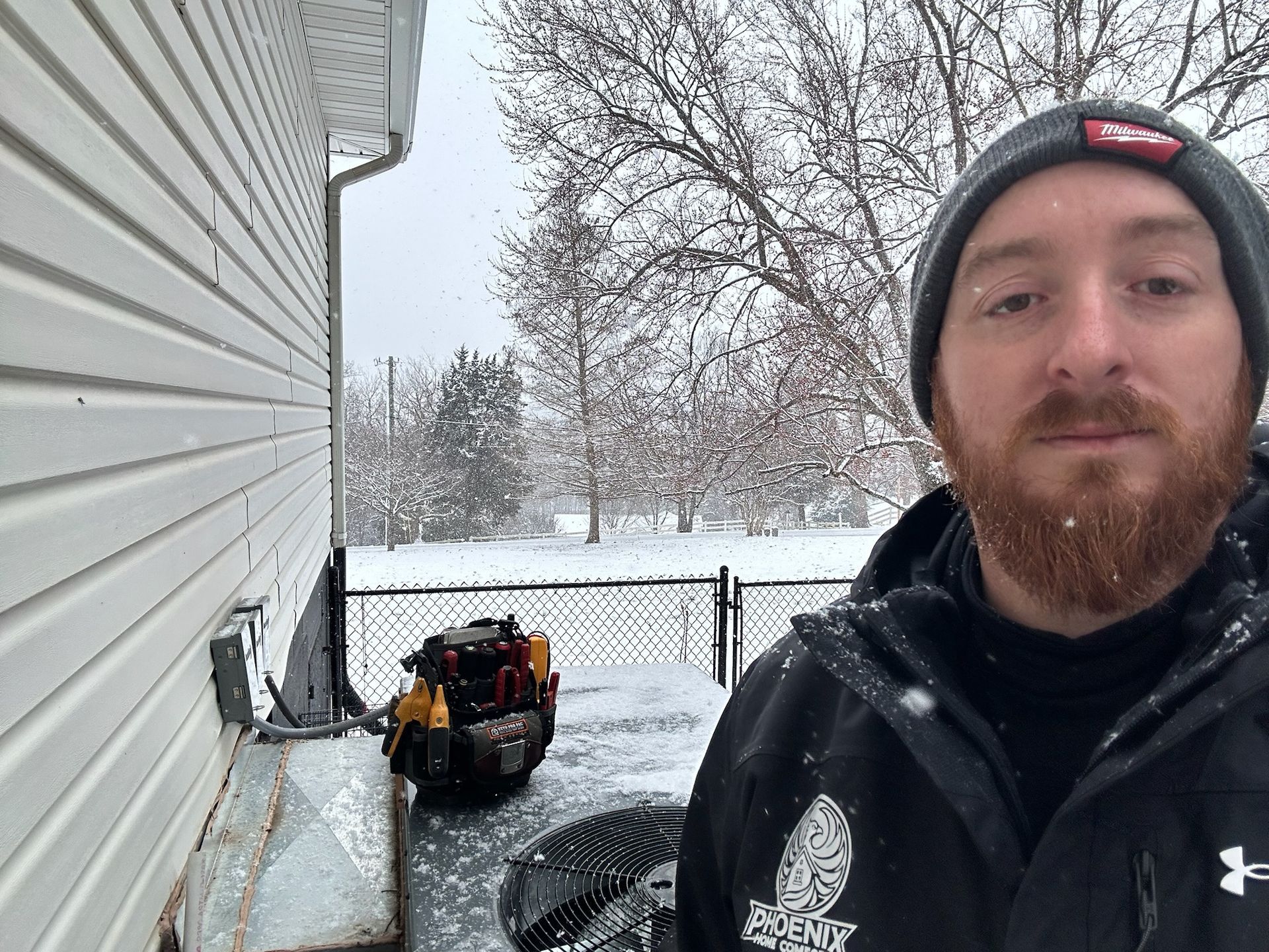 Man in winter gear beside an outdoor unit, snow falling.