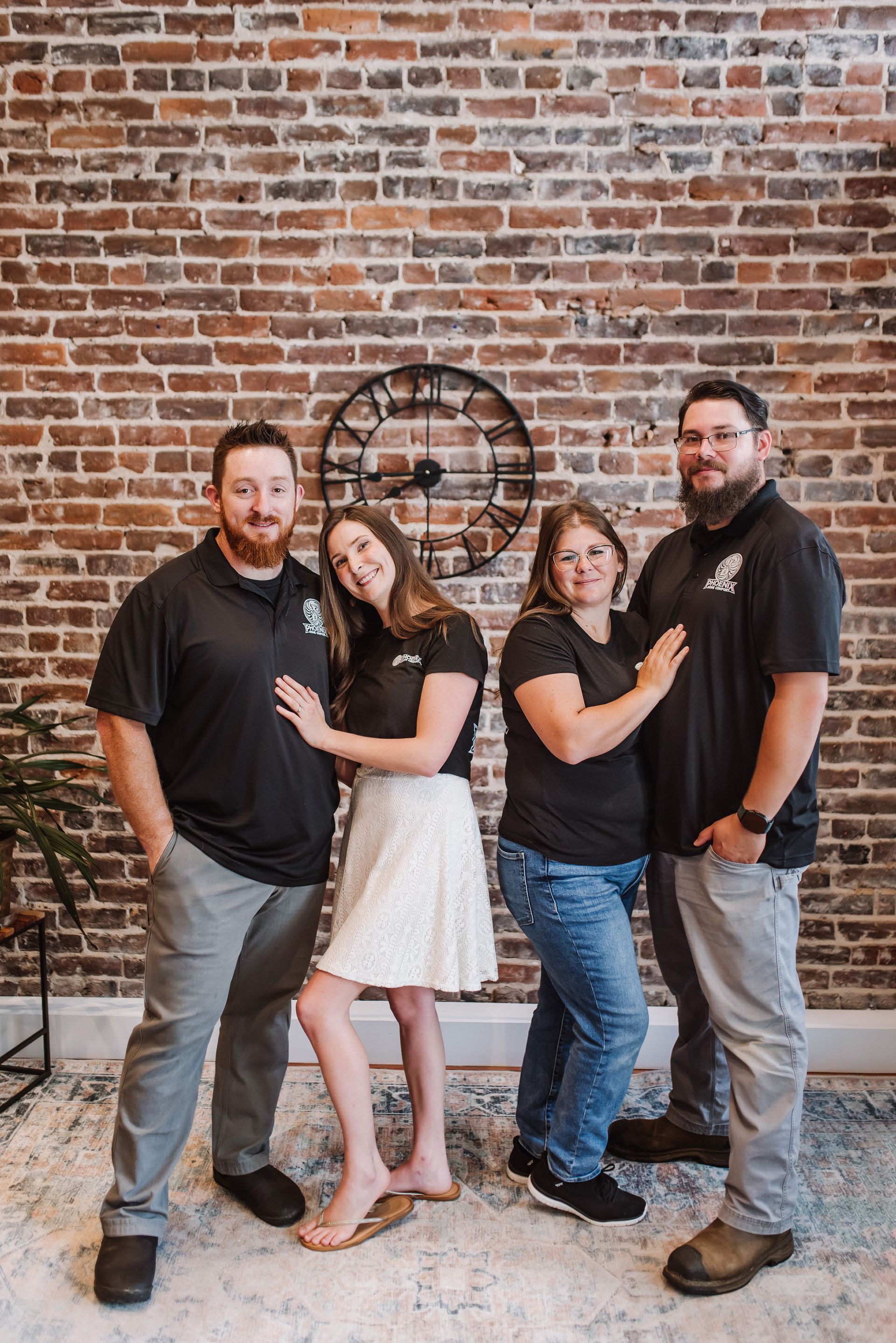 Four people posing together in front of a brick wall, smiling and hugging.