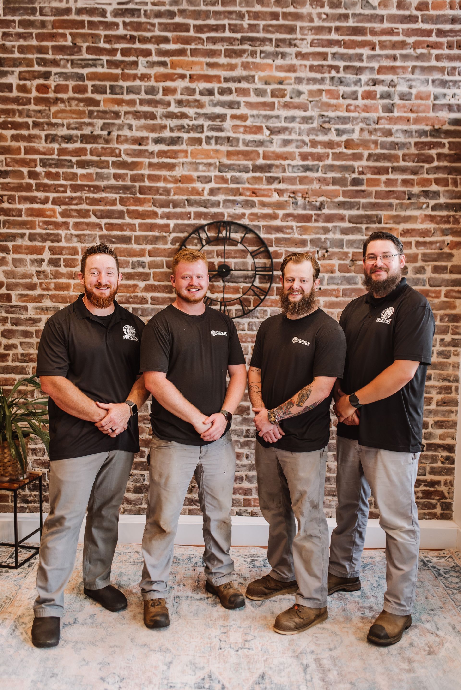 Four people in black shirts and jeans standing together in front of a brick wall
