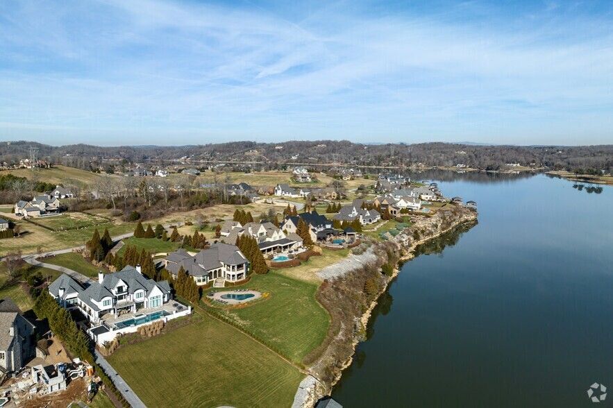 Aerial view of a lakeside neighborhood with houses, green lawns, and calm water under a clear blue sky Aerial view of a lakeside neighborhood with houses, green lawns, and calm water under a clear blue sky