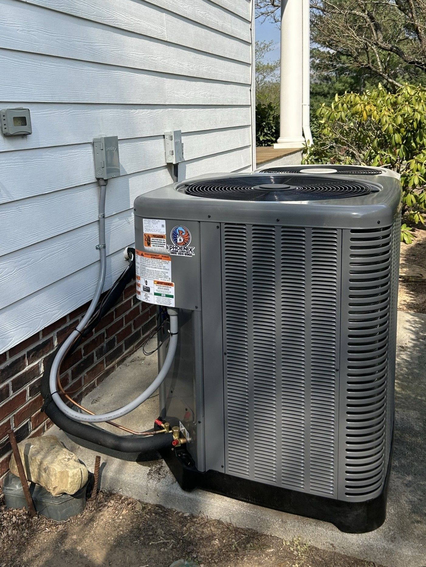 Outdoor air conditioner condenser unit beside a house wall with attached refrigerant lines and electrical conduit