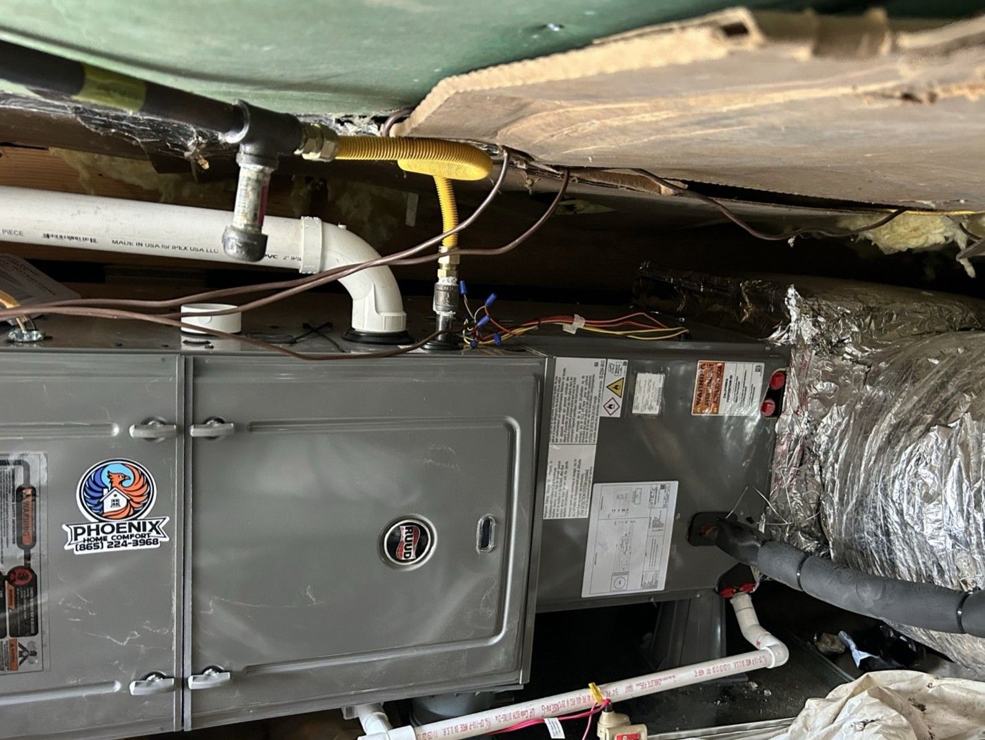 Gray furnace in a crawlspace with exposed ducts, pipes, and wiring under the floor