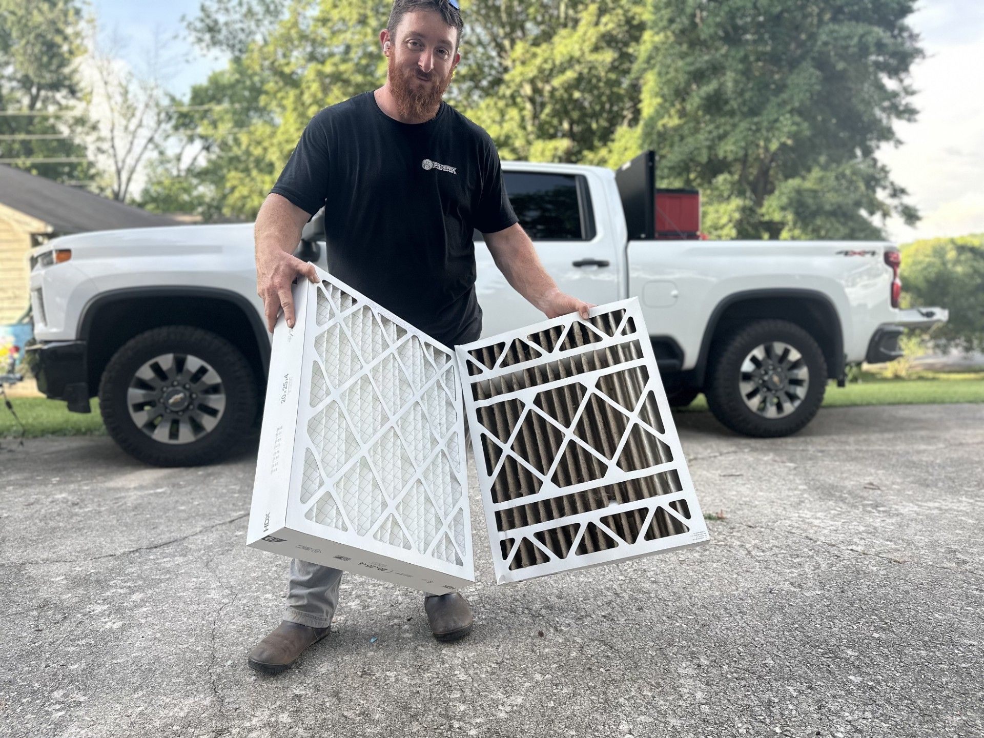 Man holding two white lattice panel sections in a driveway beside a white pickup truck