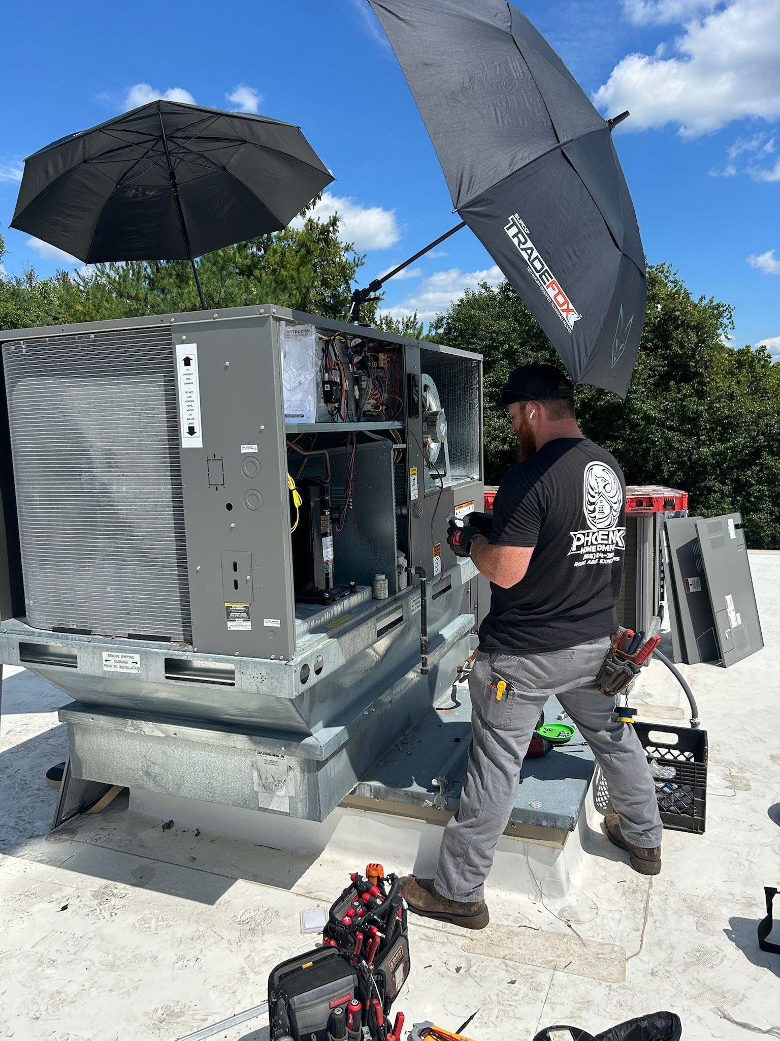 Technician inspecting outdoor HVAC unit on a rooftop, with sun umbrellas and equipment nearby