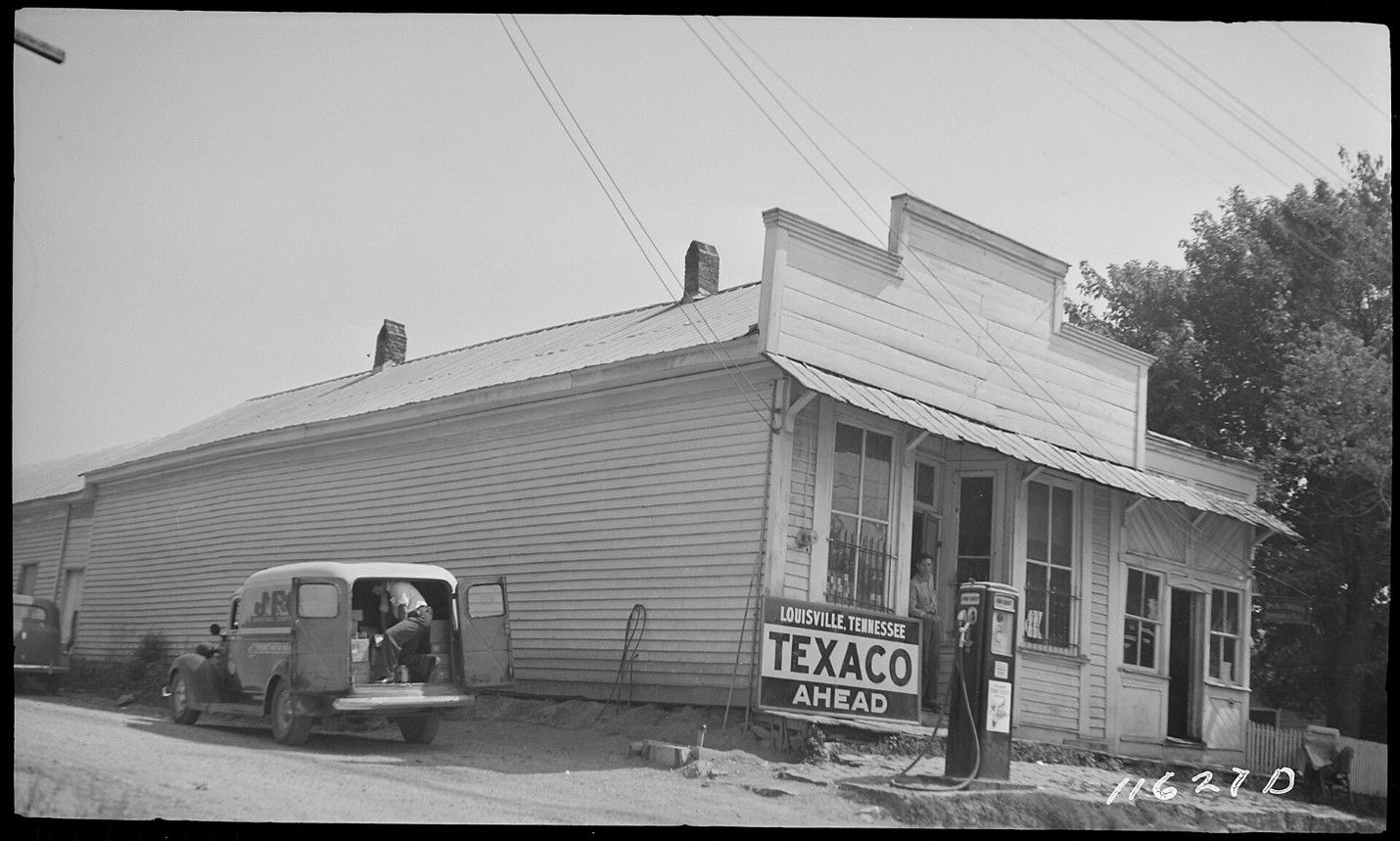 Old Texaco gas station with a parked van and a person standing by the sign