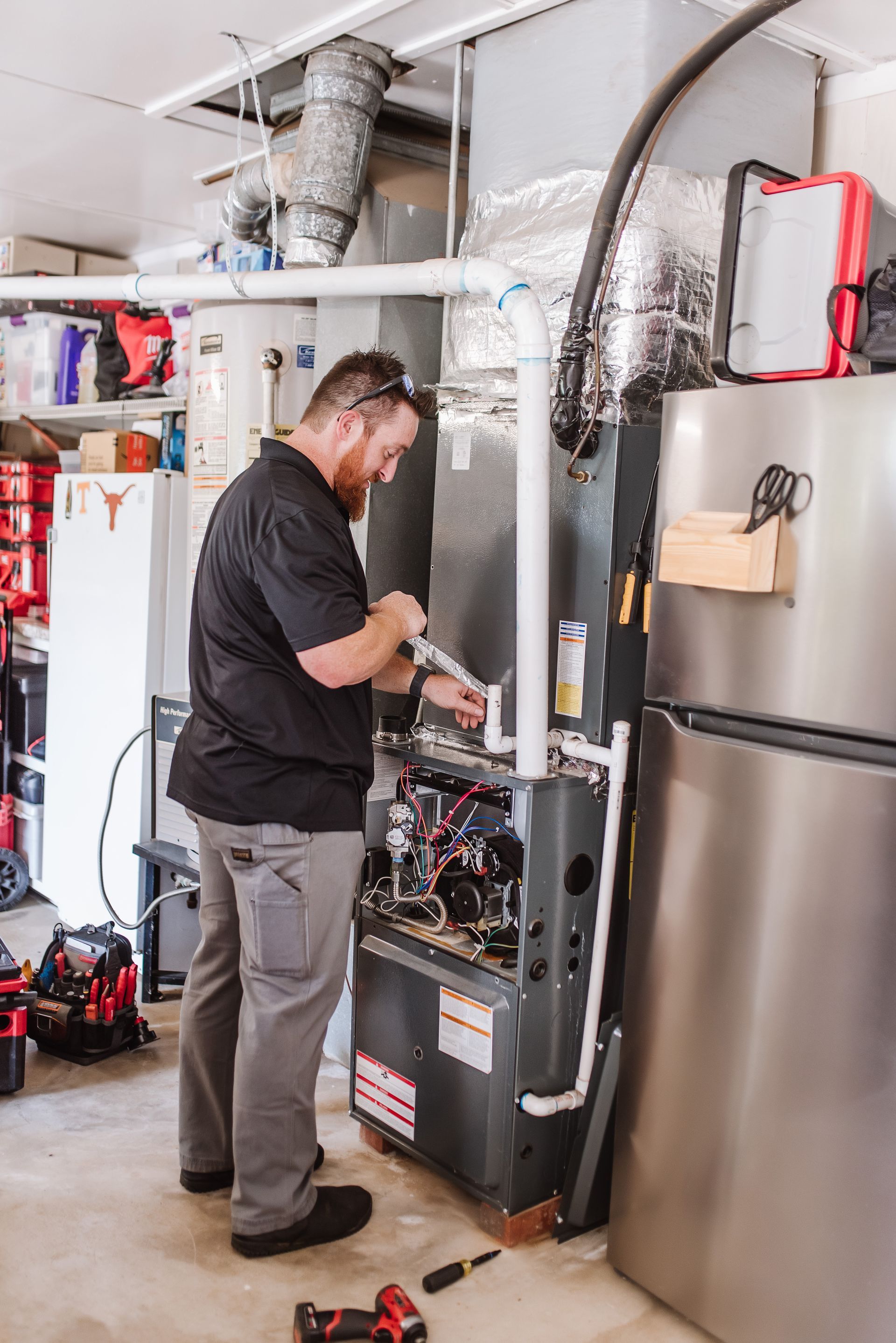 Technician inspecting a furnace beside a stainless steel refrigerator in a home utility area
