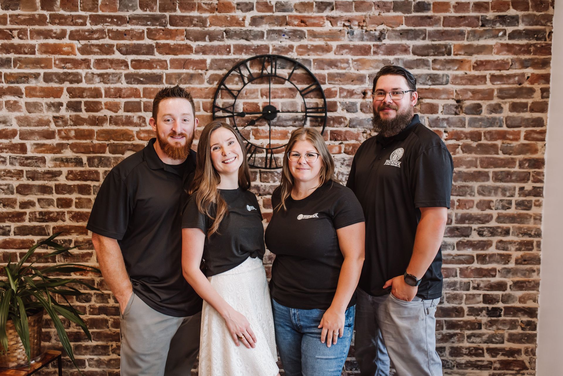 Four people posing in front of a brick wall, wearing black shirts and jeans.
