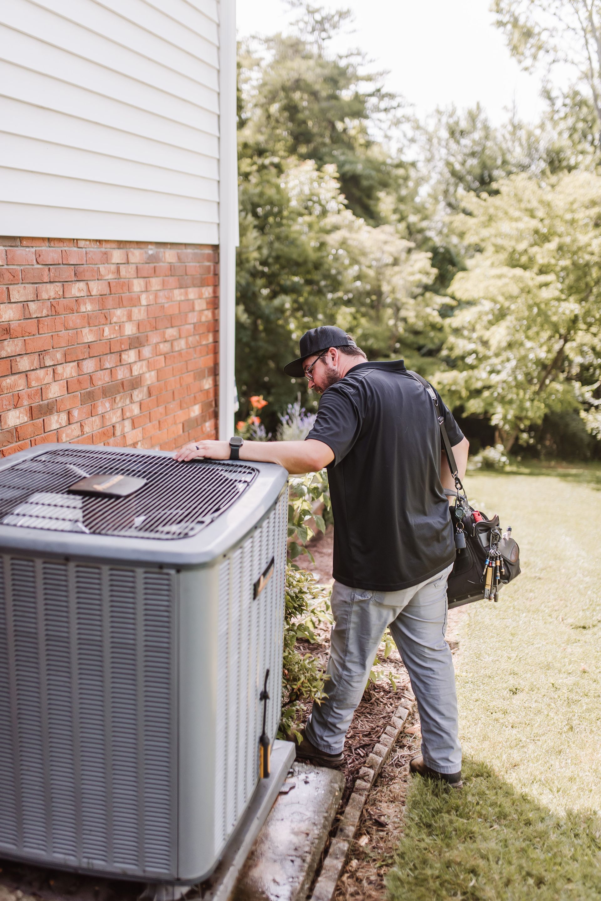 Technician inspecting an outdoor HVAC unit beside a house