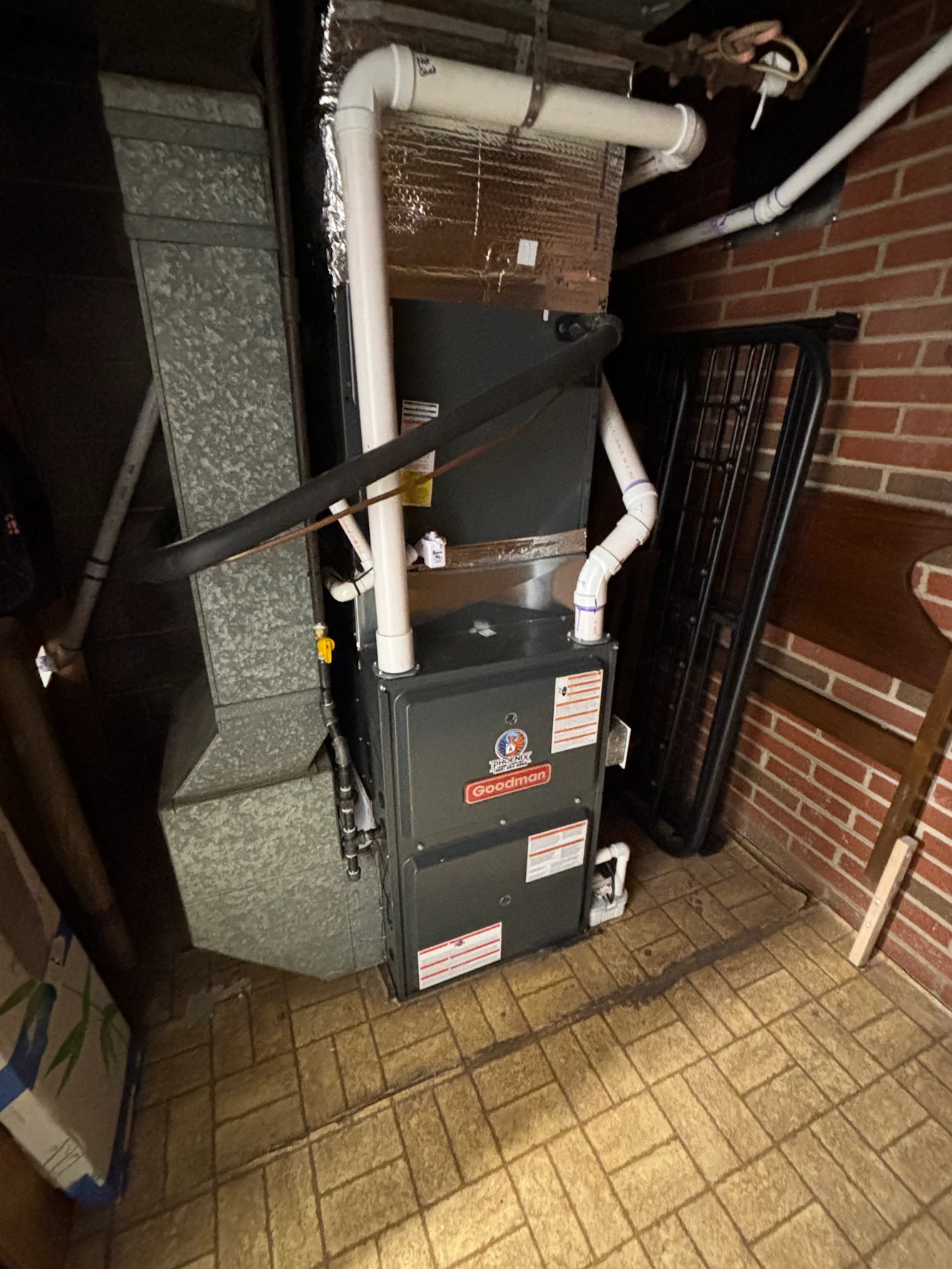 Furnace and HVAC unit in a narrow utility room beside brick walls and exposed ductwork.