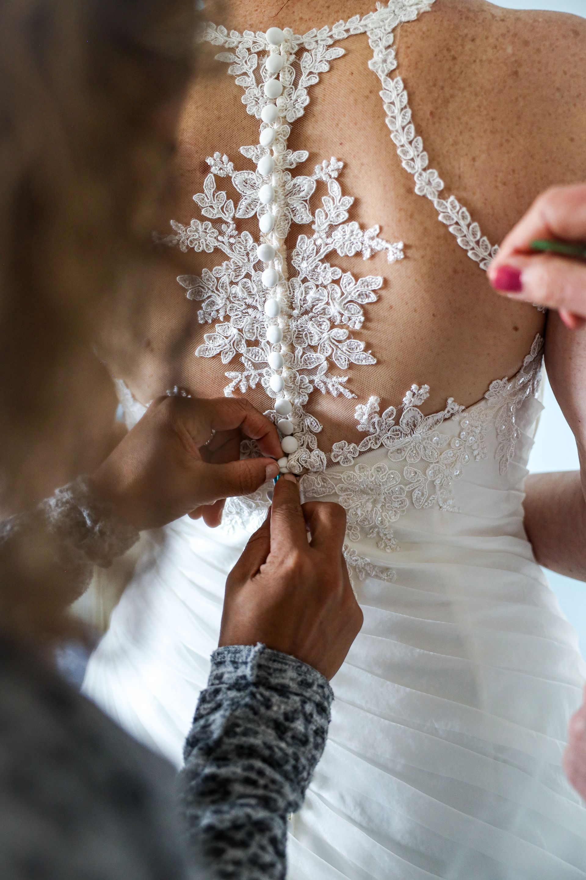 Handen maken de rits van een witte kanten trouwjurk op de rug van de bruid dicht. Bruidsjurk. Bruidsfotograaf.