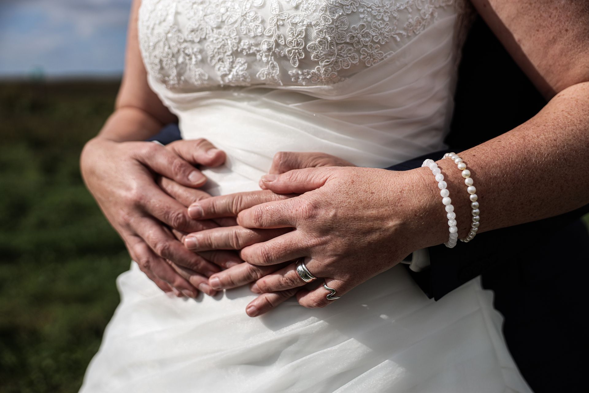 Handen om de taille van een witte trouwjurk geklemd, buitenlocatie. Bruiloft fotografie. Bruiloft fotograaf.