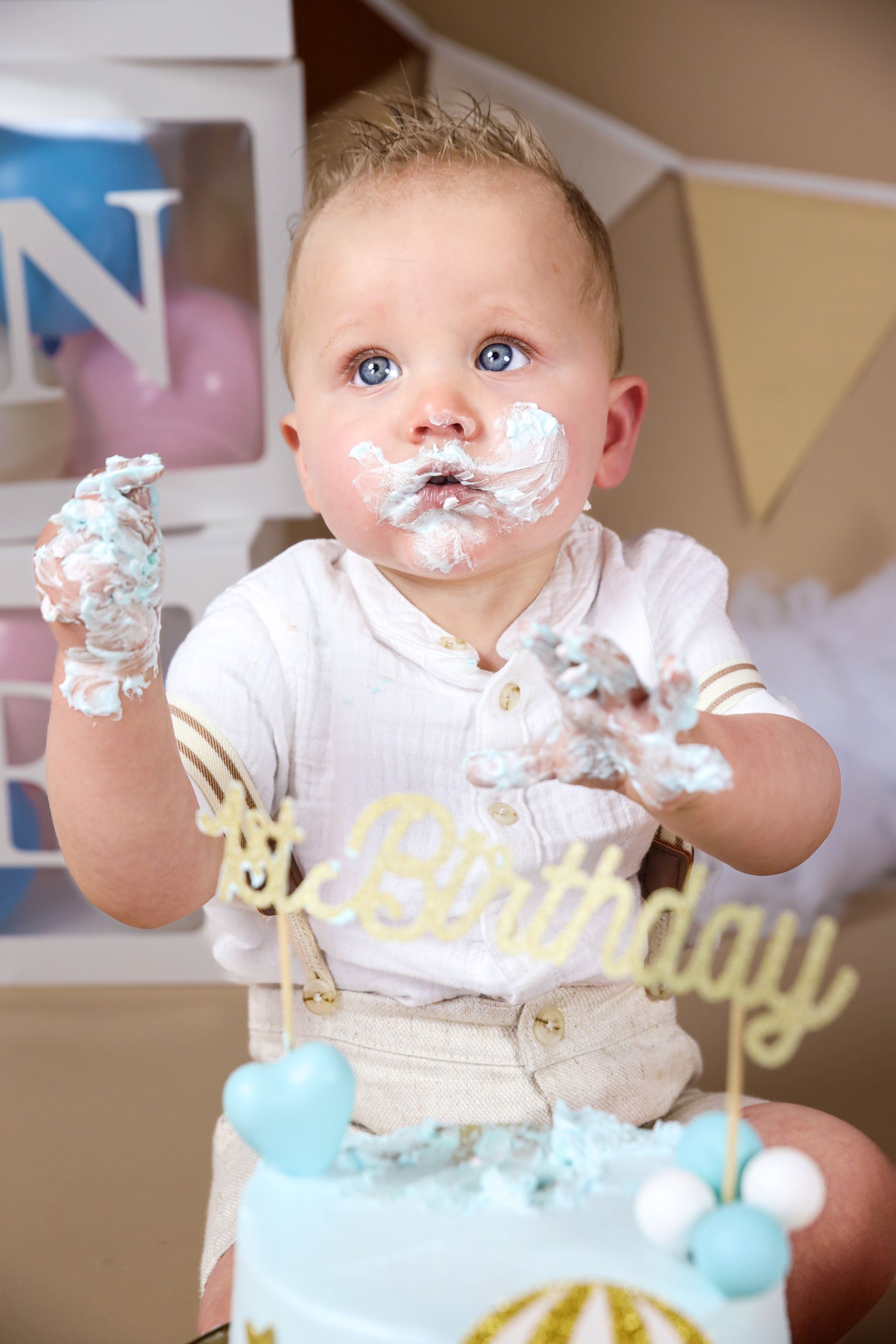 Een baby, helemaal onder de taart, zit bij een cakesmash fotoshoot voor een eerste verjaardag. Smashtaart, eerste verjaardag.