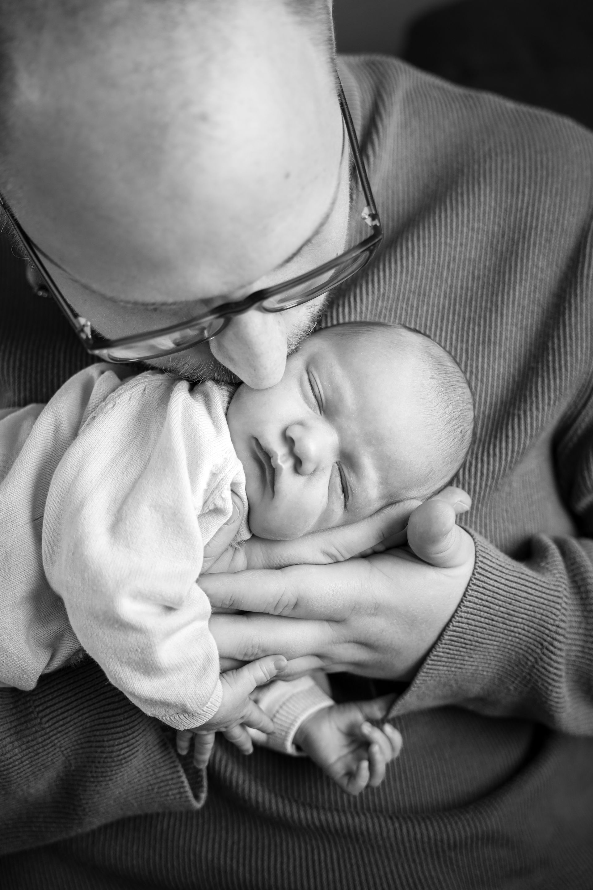 Een volwassene wiegt een slapende baby dicht tegen de borst, beiden in een close-up. Newbornfotograaf Hellevoetsluis.