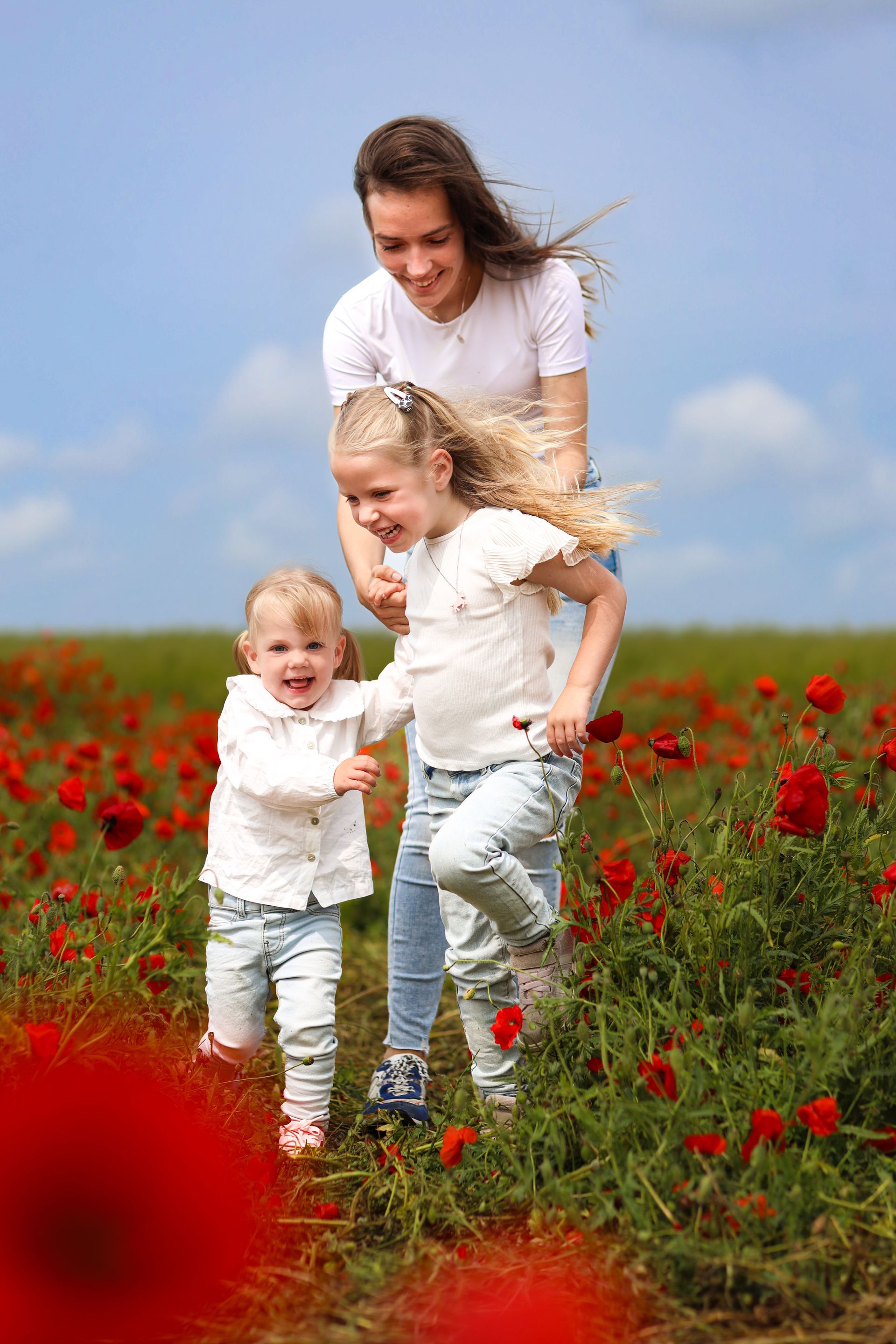 Vrouw en twee kinderen in een veld met rode bloemen onder een blauwe hemel. Kinderfotografie Zuidland. Kinderfotoshoot.