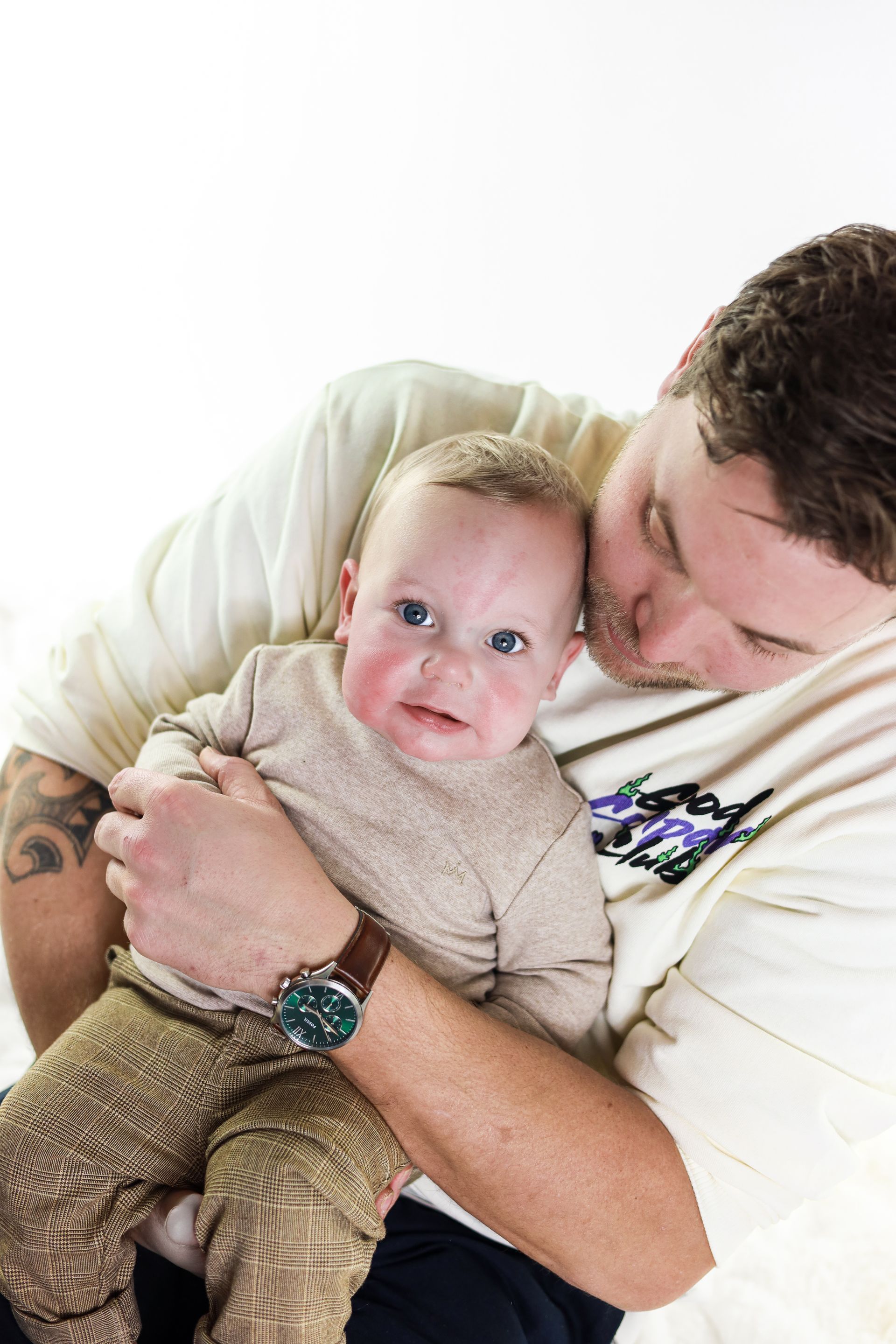 Man die een baby vasthoudt en het hoofdje van het kind kust, tegen een witte achtergrond. Vader zoon fotoshoot.